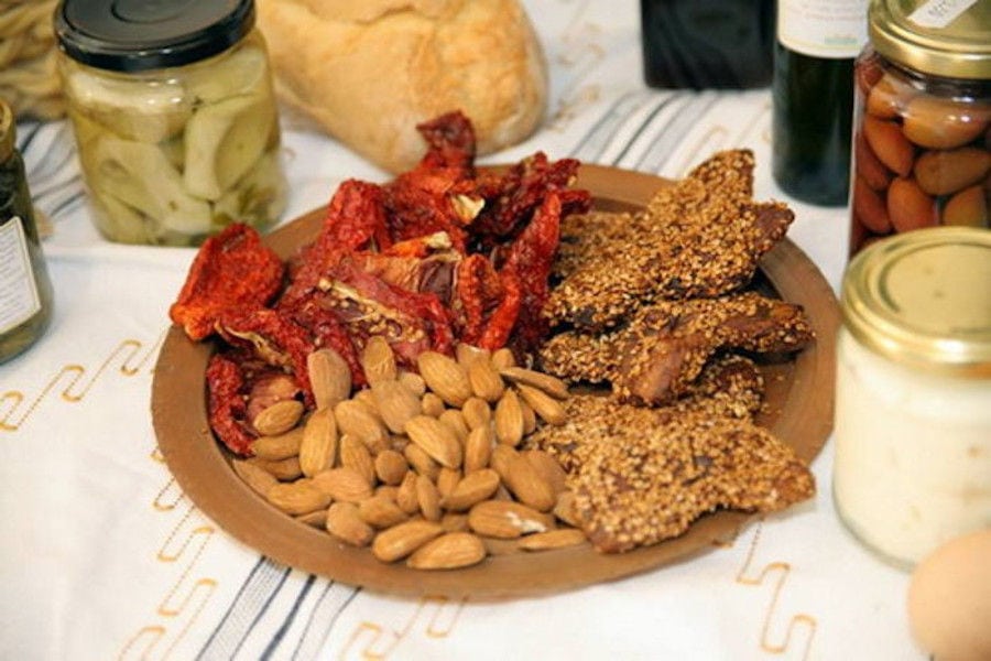 wooden plateau with sundried tomatoes, almonds surrounded by jars with olives and pickles at 'Aristaios' store
